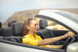 Mulher dirigindo com os cabelos ao vento em um dia ensolarado, transmitindo sensação de liberdade e prazer ao volante.